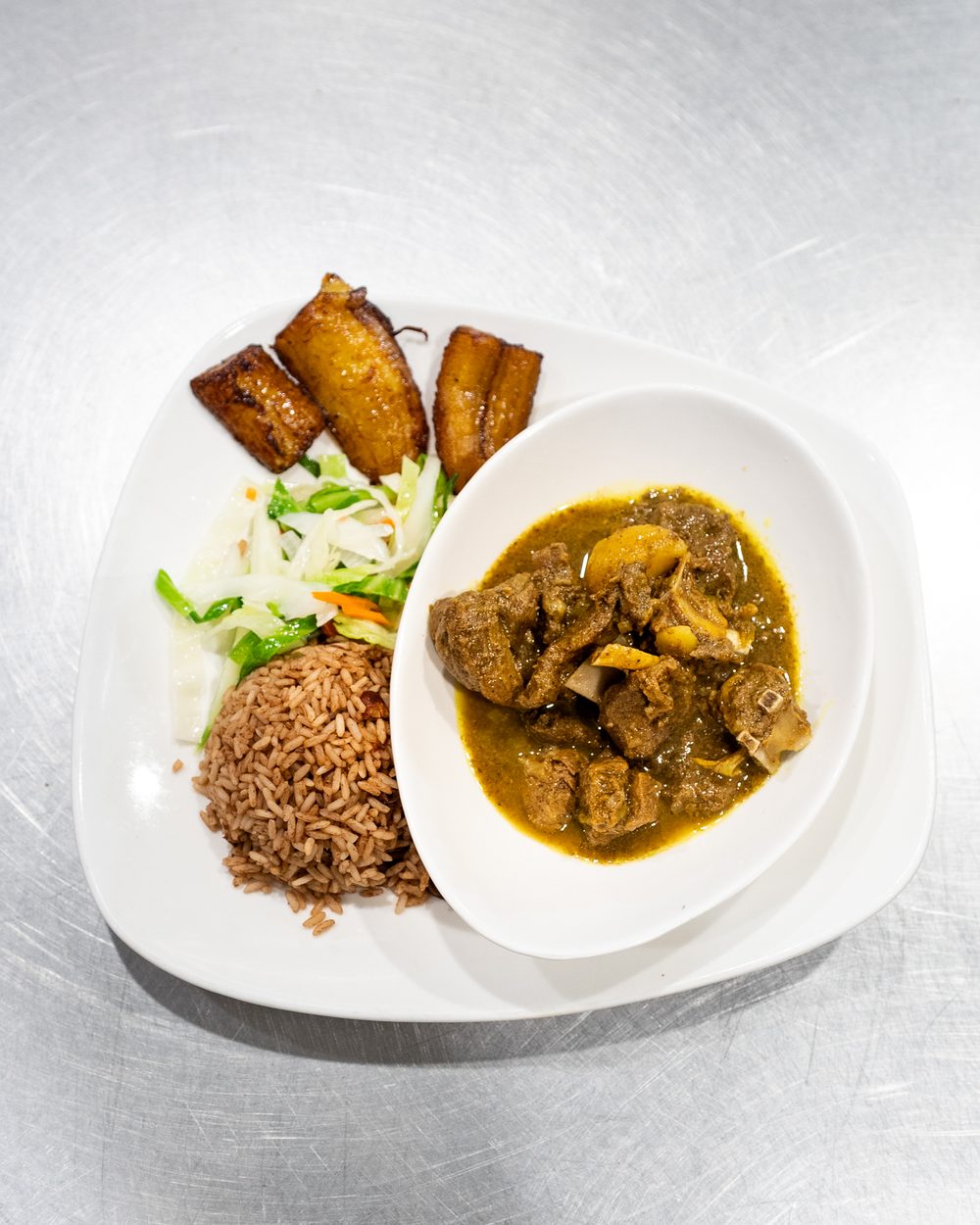Tru Jamaica curry goat with rice and peas, steamed cabbage, and sweet plantains